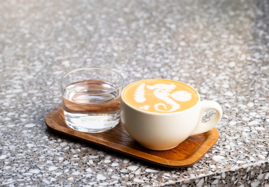 A flat white with latte art and a glass of water on a wooden tray