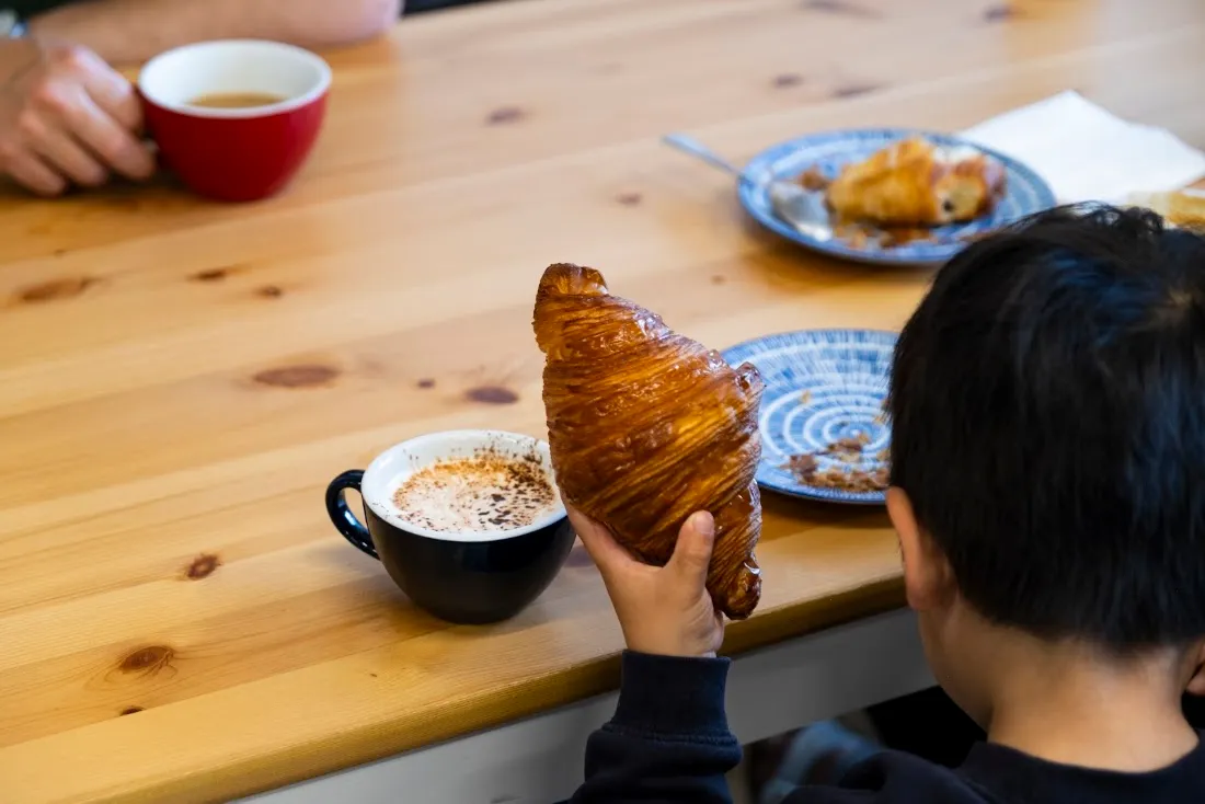 A customer holding a croissant next to a flat white