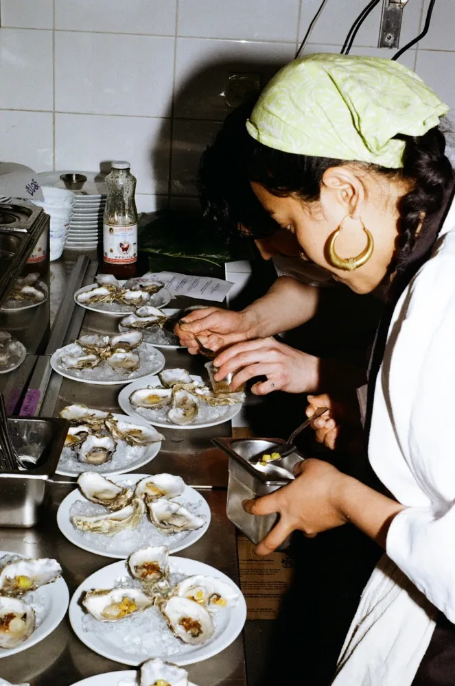A chef plating small dishes on a busy pass