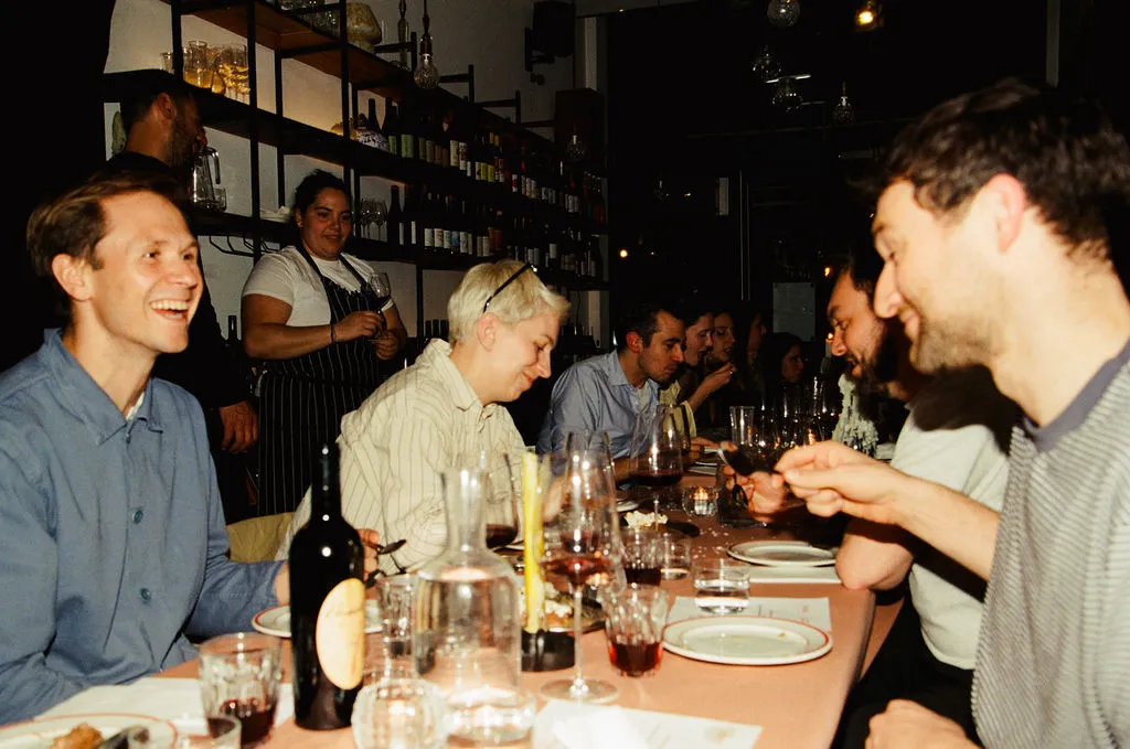 Diners laughing around a long table at a supper club