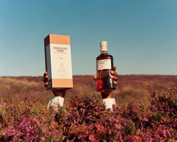 A whisky bottle and its gift box held up in a field of purple heather